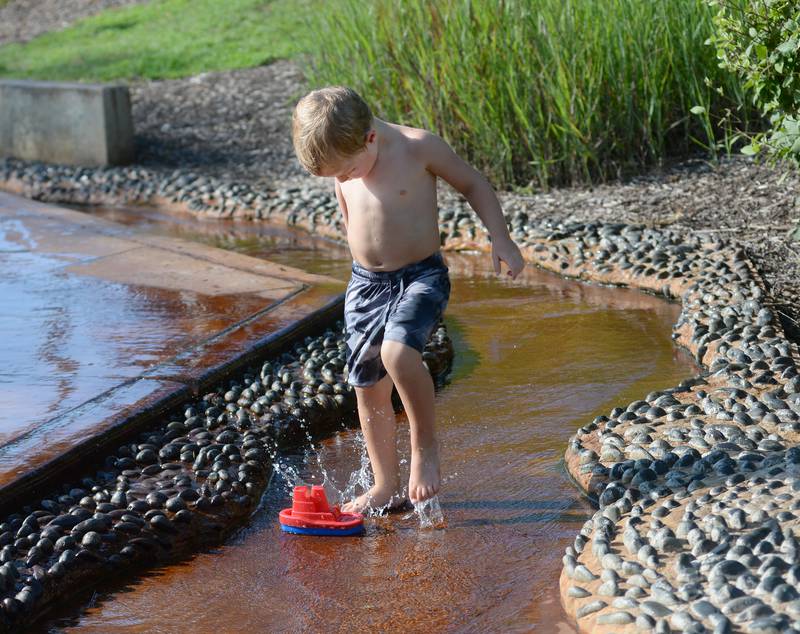 Asa Schuler, 3, of Oregon, creates waves to move his plastic boat down the "river" at the Oregon Park District's Splash Park at Park West on Monday, July 28, 2025.