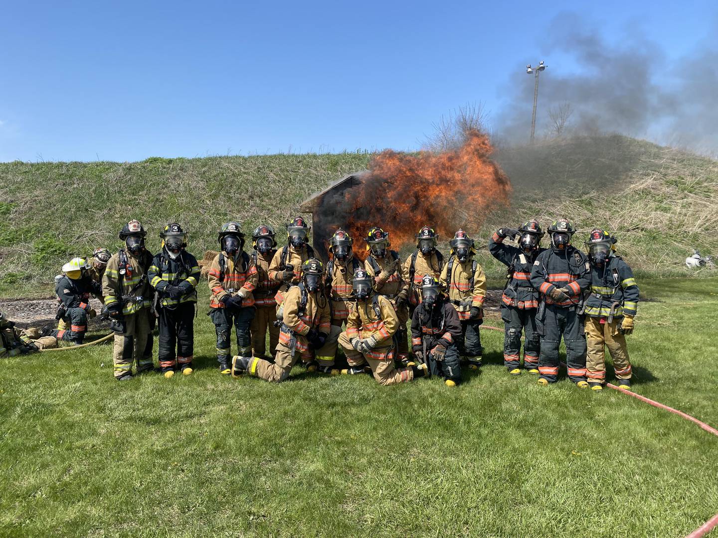 Grundy Area Vocational Center students pose next to one of the burning structures at the 2023 live burn. Every year, the fire science students participate in a live burn of one of the structures built by the students participating in the construction courses.