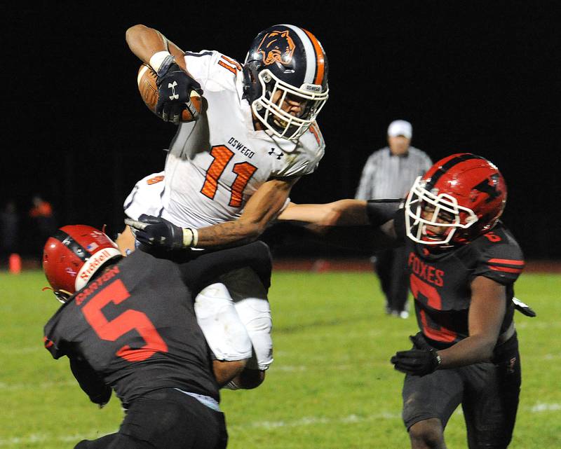 Oswego runningback Mark Melton (11) jumps between Yorkville defenders Andrew Garton (5) and Isiah Griffin (6) during a varsity football game at Yorkville High School on Friday.
