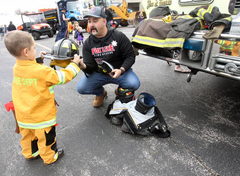 Joseph Adams, 4, of Ingleside gets some help from Joe Ugaste, firefighter/paramedic with the Fox Lake Fire Protection District, putting on a real firefighters helmet during the Halloween Howl at the Village of Fox Lake Police Department.