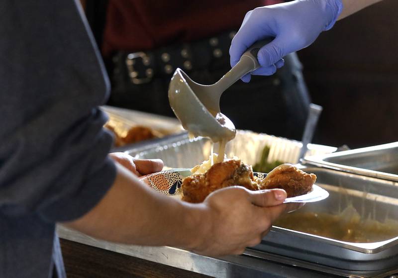 Gravy is poured on fried chicken during a free pre-Thanksgiving luncheon on Wednesday, Nov. 22, 2023, at the Woodstock train depot. This is the second year the meal that was provided through efforts of Warp Corps, MBI Cares, Isabel’s Family Restaurant, and Napoli’s Pizza, all located in Woodstock