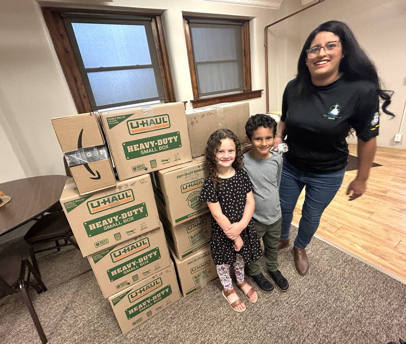 John and Eliana Murphy, ages 5 and 7, and their mom Michelle, stand by the boxes filled with care packages headed for sailors on the USS Fitzgerald. Volunteers assembled the care packages  at the Evangelical Free Church of Mt. Morris  on Thursday, Oct. 16, 2025. Michelle's husband and John and Elaine's dad, Logan, is the chaplain for the destroyer.