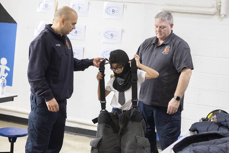 Sterling Firefighters Adrian Avelar (left) and Dave Northcutt help 3rd grader Caden Saguilla try on equipment Monday, Jan. 29, 2024 at St. Mary’s School in Sterling. Along with learning about different professions, students were allowed to wear clothing to match what they want to be when they grow up.