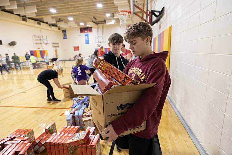 Caleb Carlson (right), 15, hauls a box of food with the help of Jack Redell, 14, after being loaded up Tuesday, Dec. 20, 2022 at the Dixon YMCA.