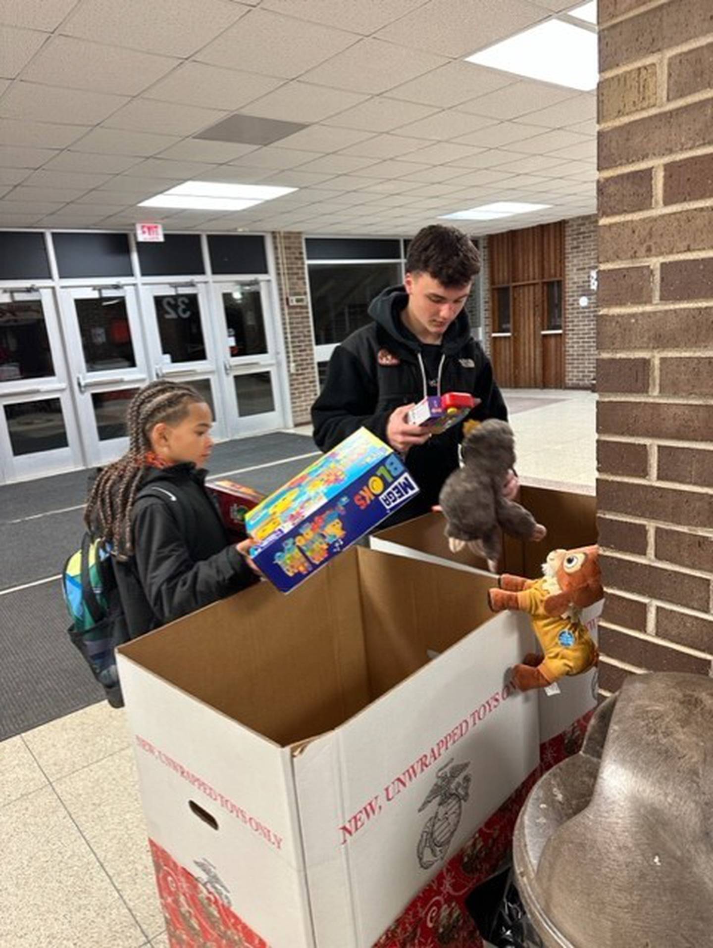 (From left) Silas Hernandez, 7, and Carson Beach, 15, place toys in a donation box for the 2024 Guns and Hoses charity basketball game on Monday, Dec. 4, 2024, in DeKalb. The game pitted DeKalb School District 428 educators and staff with first responders from DeKalb city police and fire departments, benefiting DeKalb County Marines toy collection.