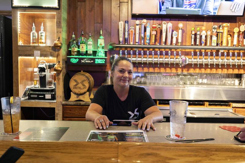 Autumn Halvorsen, general manager/team leader of X-Golf Sauk Valley, smiles from behind the bar Thursday, August 7, 2025.