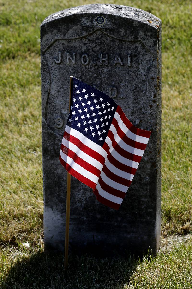 Sunlight illuminates an American Flag at a veterans grave in the St. John the Baptist Cemetery,
