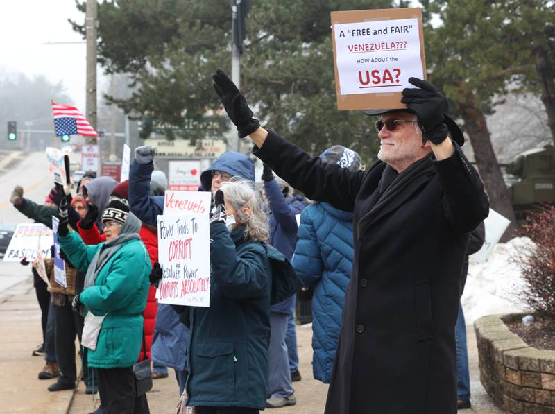 Protesters wave as cars honk in support Tuesday, Jan. 6, 2026, during a Venezuela Rapid Response Rally at Memorial Park on the corner of First Street and Lincoln Highway in DeKalb. The group gathered to voice their opposition to President Donald Trump and the administrations recent actions in Venezuela.