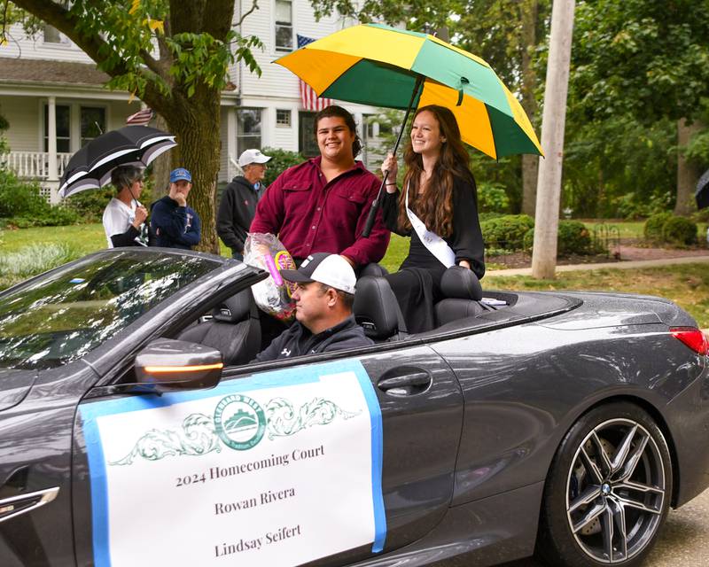 Glenbard West homecoming court members Lindsay Seifert and Rowan Rivera try to stay dry and pass out candy on Saturday Sept. 28, 2024, while the parade travels down main street to Glenbard West High School.