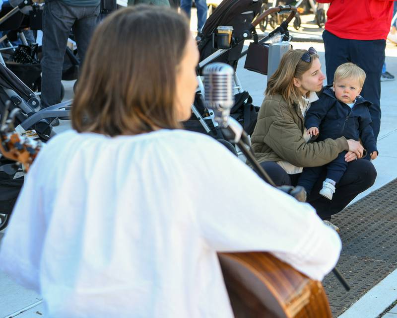 Tammy and her 19 month old son Owen listen to Annalee Hooson of Wheaton during the Wheaton French Market on Saturday April 13, 2024, in downtown Wheaton.