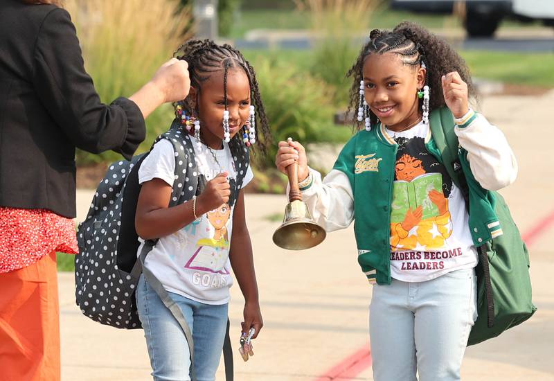 DeKalb School District 428 Superintendent Minerva Garcia-Sanchez lets Gwendolyn Brooks Elementary School students Naomi Patton, (left) a third grader, and Eboni Allen, a fourth grader, ring the bell as they arrive at the school Thursday, Aug. 17, 2023, for the first day of the new year.