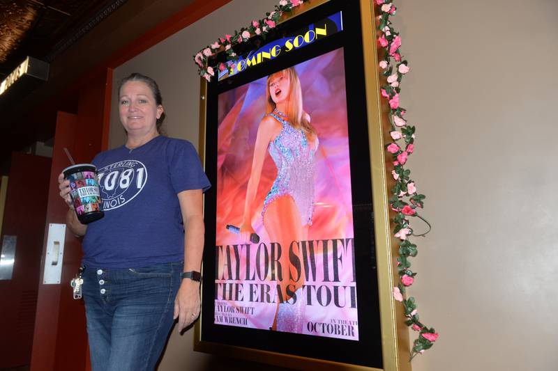Lori VanOosten, the general manager for the Sterling Theater, stands by one of the movie posters for Taylor Swift's "The Eras Tour" while holding a commemorative cup. The popular movie premiered at theaters last week to enthusiastic crowds.