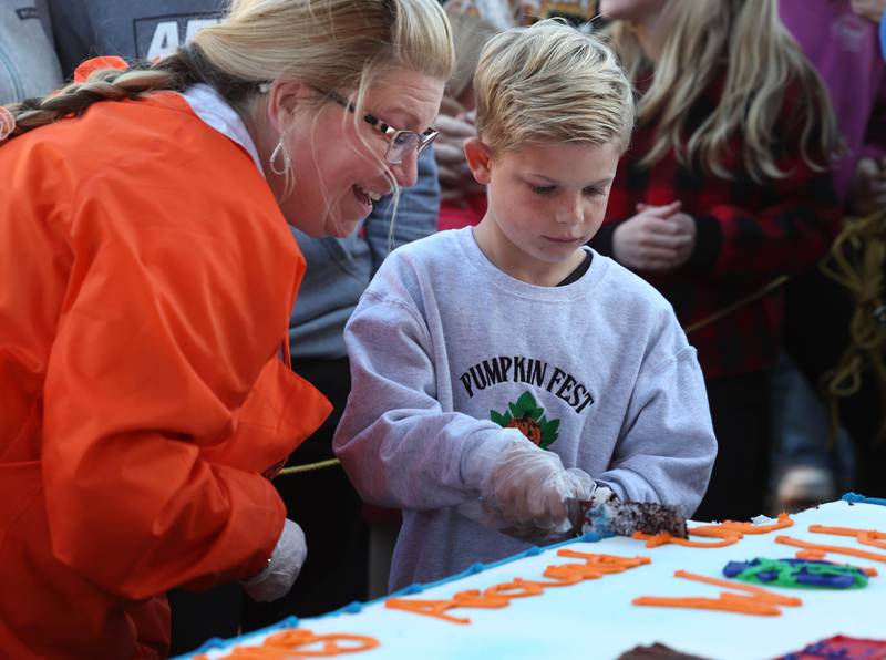 Brandi Voigt, theme director of the Pumpkin Fest Committee, helps Theme Contest honorable mention winner Jaxson Ruby cut the cake Wednesday, Oct. 23, 2024, on North Maple Street adjacent to the DeKalb County Courthouse during the Sycamore Pumpkin Festival.