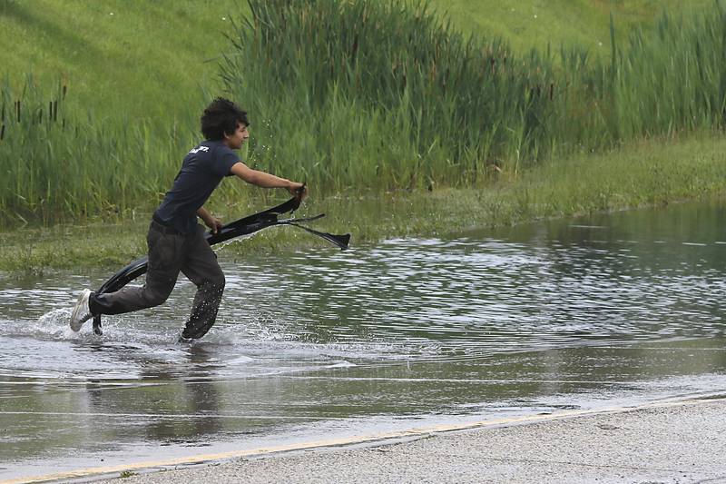 A motorist retrieves part of his car from a  section of high water on Illinois Route 14, near Nimco Drive, on Tuesday, June 25, 2024, after heavy rain from overnight thunderstorms.