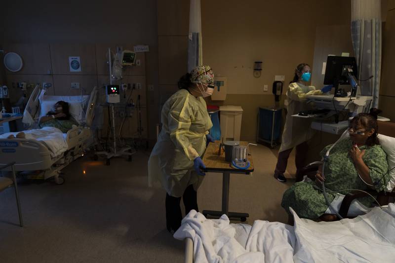 Registered nurse Nvard Termendzhyan, center, sets up a table for Linda Calderon, right, as her twin sister Natalie Balli, far left, rests in her bed in a COVID-19 unit at Providence Holy Cross Medical Center in Los Angeles, Monday, Dec. 13, 2021. The sisters were admitted to the hospital on the same day, a few days after their Thanksgiving gathering.