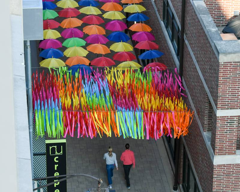 Community members walk underneath hanging umbrellas on Saturday May 31, 2025, at Schiller Court during the Elmhurst Summer Kick Off Party held at City Centre Fountain Plaza in Elmhurst.