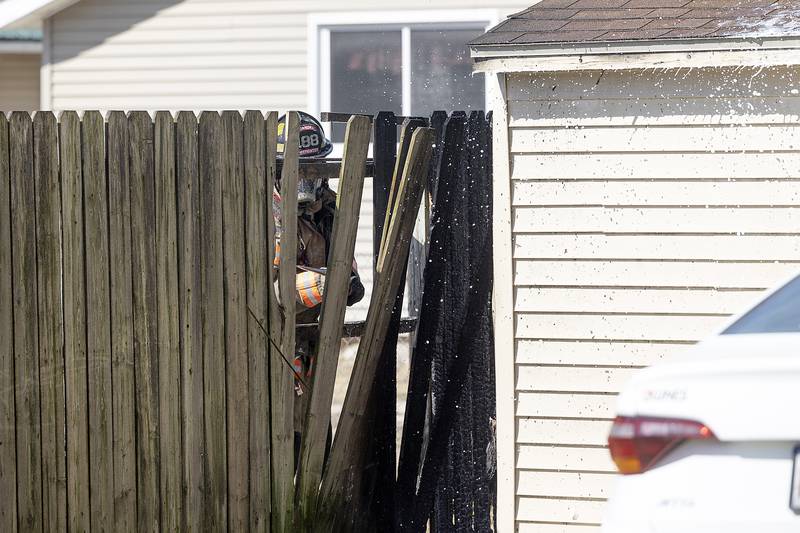A fire singed fence is dismantled as firefighters work to douse the flames on a backyard shed in Dixon on Friday, March 14, 2025.