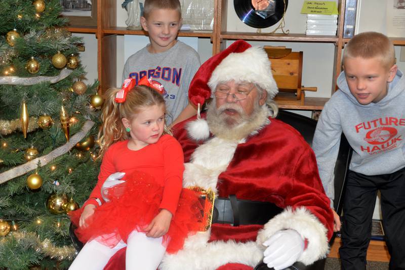 Blair Groenhagen, 5, sits on Santa's lap as her brothers Callum, 10, and Lane, 9, listen in during their visit at the  Oregon United Methodist Church's Kid's Christmas Carnival during Oregon's Candlelight Walk on Saturday, Nov. 30, 2024.
