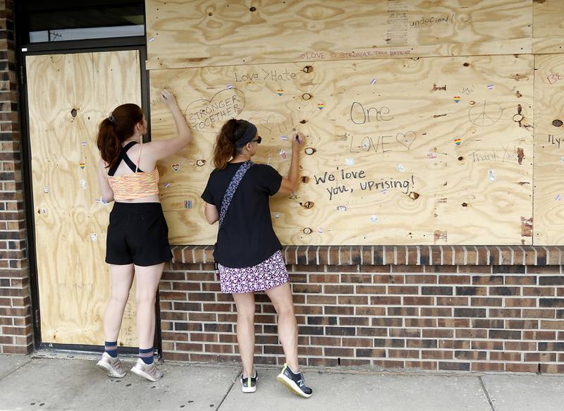 Jacqui Murk, right, of Crystal Lake, and her daughter, Izzie, write notes of support on the boarded up window at Uprising Bakery & Cafe in Lake in the Hills, on Monday, July 26, 2022, after the store reopened Sunday after its front windows were smashed and epithets written on the walls, to long lines and enthusiastic community support. The cafe, which was planning to host an all-ages drag show Saturday night, had experienced backlash over the previous few weeks.