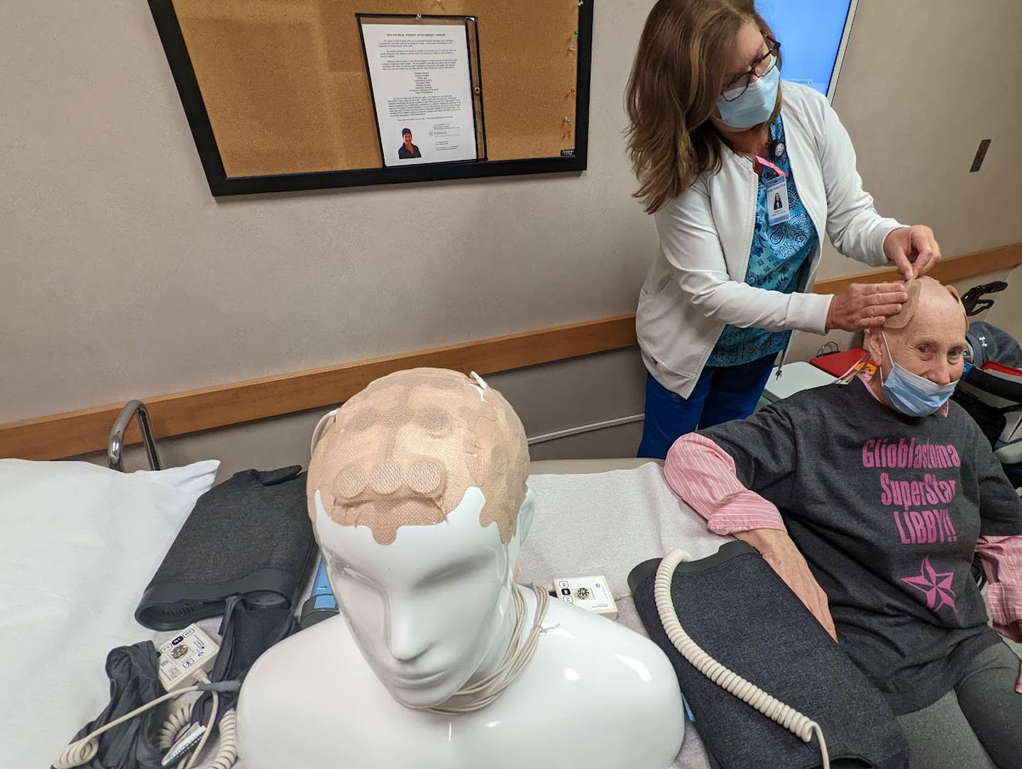 Joan Quaresima, a radiation oncology nurse at Joliet Oncology-Hematology Associates, applies transducer arrays to the scalp of Libby Hall, 75, of Joliet, on Friday, Sept. 16, 2022. Hall was diagnosed with glioblastoma multiform, an aggressive brain cancer, in 2020 and is currently wearing a device called Optune, which delivers an electrical field into the cancer cells in her brain. A teaching model is seen in the foreground.