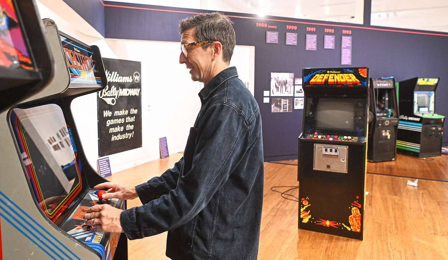 Curator Justin Witte tests out the “Robotron” machine as preparations continued Thursday for the opening of the “INSERT COIN: Inside Midway’s Arcade Revolution” exhibition at the College of DuPage.