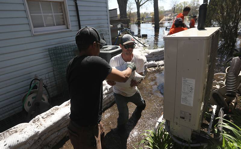Jai Hale hands a sandbag to Ryan Downey as the works to sandbag Downey’s home with McHenry Home Depot volunteers as flooding continues on the Fox River on Wednesday, April 22, 2026, near Burton’s Bridge.