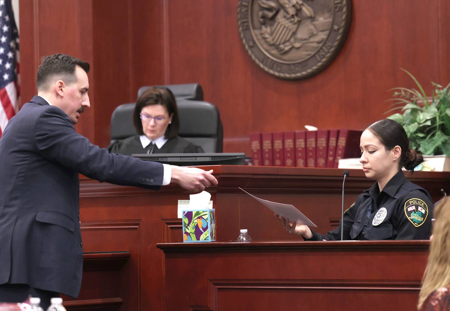 Special prosecutor Derek Dion hands a piece of evidence to witness, Sycamore police officer Coraima Beltran, on Wednesday, Feb. 18, 2026, during Hamza Khatatbeh’s murder trial at the DeKalb County Courthouse in Sycamore. Khatatbeh, 17, is accused of fatally stabbing Sycamore 17-year-old Kaleb McCall in 2023.