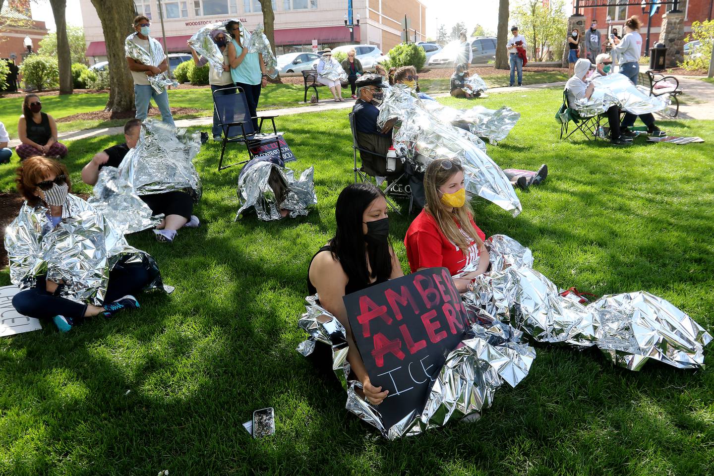 Attendees listen to speakers as some wrap themselves in a thin mylar sheet as symbolism and in solidarity with U.S. Immigration and Customs Enforcement detainees who are issued the same thin blankets while in custody. About 80 people were in attendance at the rally to end McHenry County's contract with ICE on Saturday, May 1, 2021, in Woodstock.