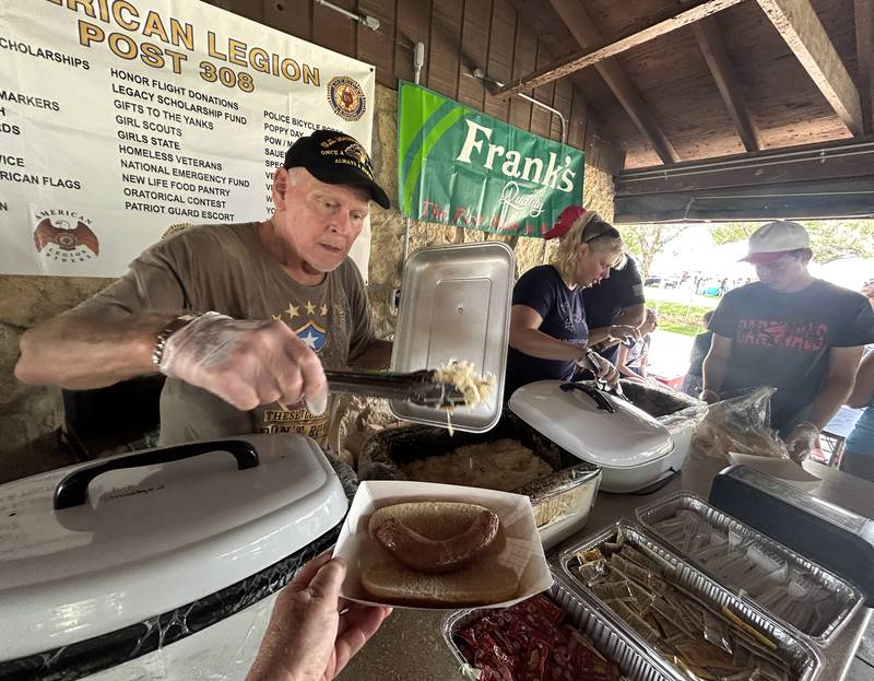 Tom Cox of the American Legion (left) and Angie Determan (center) serve brats and sauerkraut at Forreston's Sauerkraut Days on Saturday, Aug. 3, 2024. The popular luncheon was held in the shelter at Memorial Park during the three-day festival.