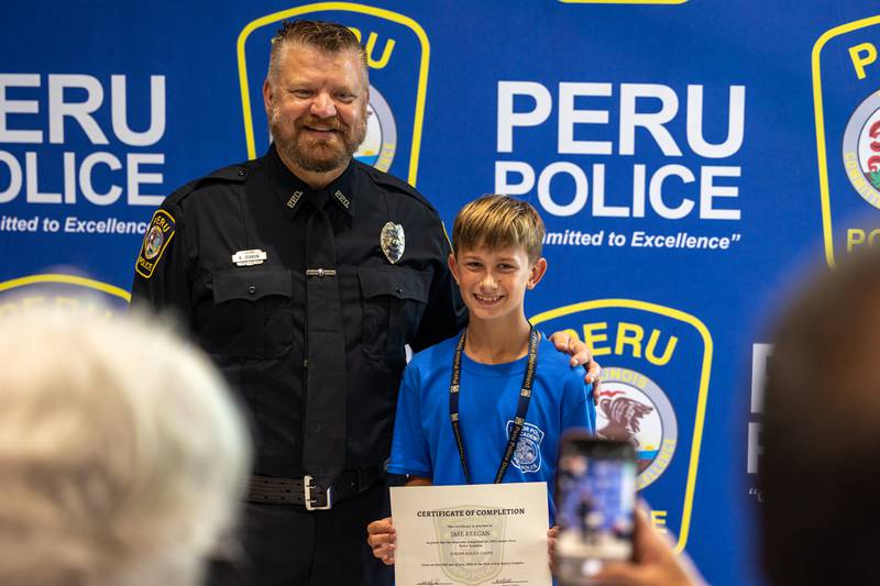 (left to right) Officer Brian Zebron and Junior Police Cadet Jase Keegan pose for photo at the first annual Juvenile Police Academy graduation ceremony on Friday, July 25, 2025 at the Peru Police Department in Peru.