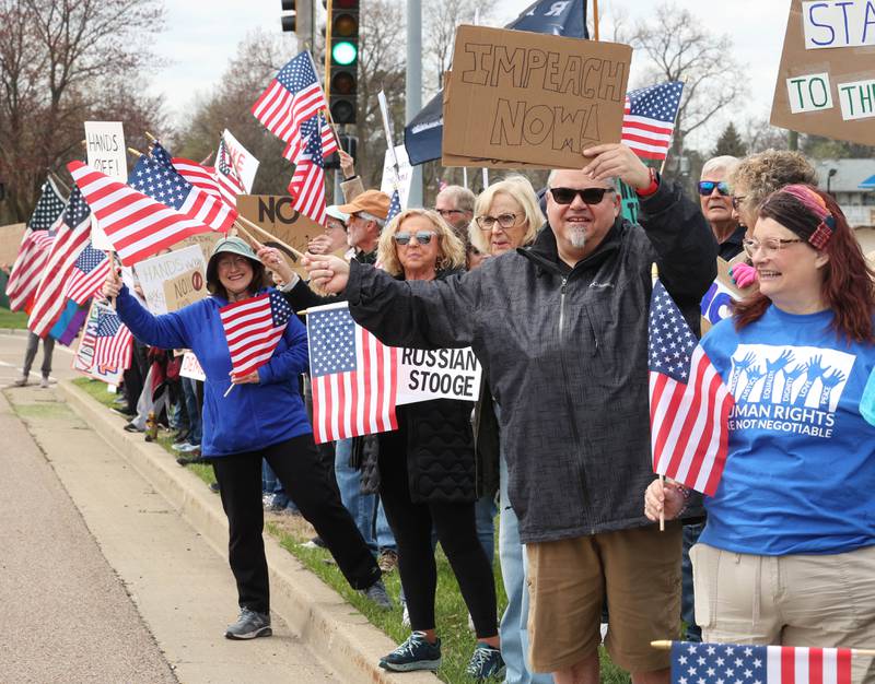 Protesters wave flags and hold signs along Sycamore Road in front of Hopkins Park Saturday, April 19, 2025, during a “No Kings” rally and march in DeKalb. The group was protesting what they’ve argued is the unlawful and harmful federal policies of President Donald Trump and his administration.