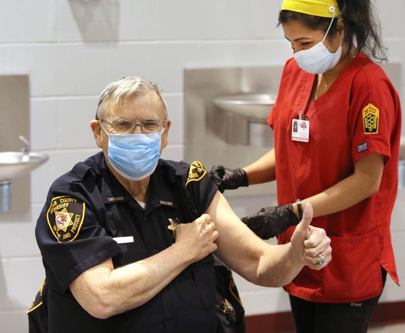 DeKalb County Sheriff Roger Scott gives a thumbs up after receiving the first of two scheduled injections of the Moderna COVID-19 vaccine from Northern Illinois University nursing student Christian Blessing Wednesday in DeKalb.