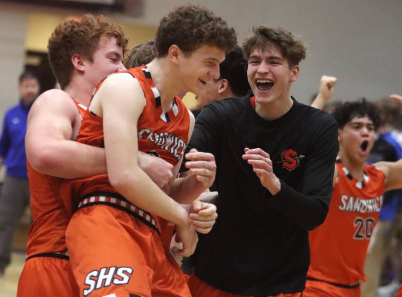 Sandwich’s Griffin Somlock, front, is embraced by teammates after draining the game-winning free throw during the OT period in varsity boys basketball on Tuesday, Feb. 11, 2025, at  Woodstock High School in Woodstock.