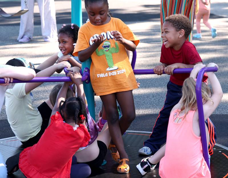 Kids ride the merry-go-round Friday, June 14, 2024, at the new playground at Hopkins Park during a Dedication Celebration event for the grand opening of the new playground and racquet courts.