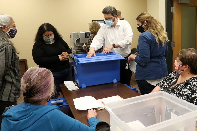 McHenry County Clerk Joe Tirio, center, reaches into a secure blue box for a handful of ballots with (clockwise from Tirio:) Kathryn Potter, Dee Darling, both of Cary, Mary Ann Brandt of Harvard, Anna Brettman of Huntley, and Stephanie Luna of Belvidere inside the voting tabulation room at the McHenry County Administrative Building on Thursday, April 8, 2021, in Woodstock.