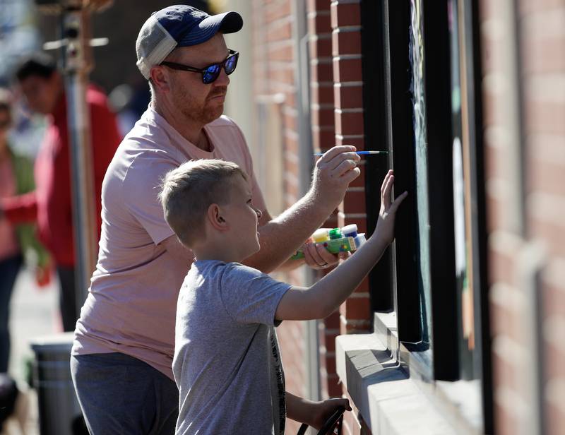 Nick Purdy and his son Will, 8, of Downers Grove paint the windows of a business in Downers Grove, Ill. on Saturday, October 22, 2022.