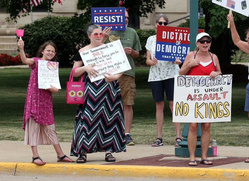 Protesters hold signs and ring bells Saturday, July 4, 2025, at the corner of Main and State Streets in front of the DeKalb County Courthouse in Sycamore for a "No Kings" rally to voice their displeasure with President Donald Trump.
