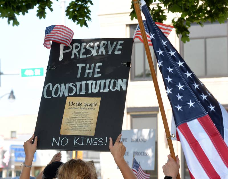 Attendees at the "No Kings" rally held in Oregon, Illinois on Saturday, June 14, 2025, hold an American flag and a sign critical of President Donald Trump.