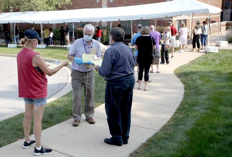 Election Judge Steve Lowe of Geneva (center) hands out voter information forms outside the Kane County Clerk's office in Geneva during the first day of early voting for the 2020 general election on Sept. 24.