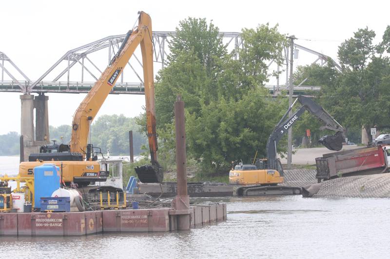Crews with Superior Sea Walls and Docks, dredge the Henry Marina on Monday, June 9, 2025 in Henry. The operation involves using an excavator on a flat barge while removing silt from the water and placing it into a smaller barge that is pushed to the shoreline by a small tug boat. 
An additional excavator will move the silt onto a tandem truck and then moved off-site. The trucks are dumping the material on a city farm located north of town. 
Once completed the Henry Yacht Club will begin installation of replacement docks.