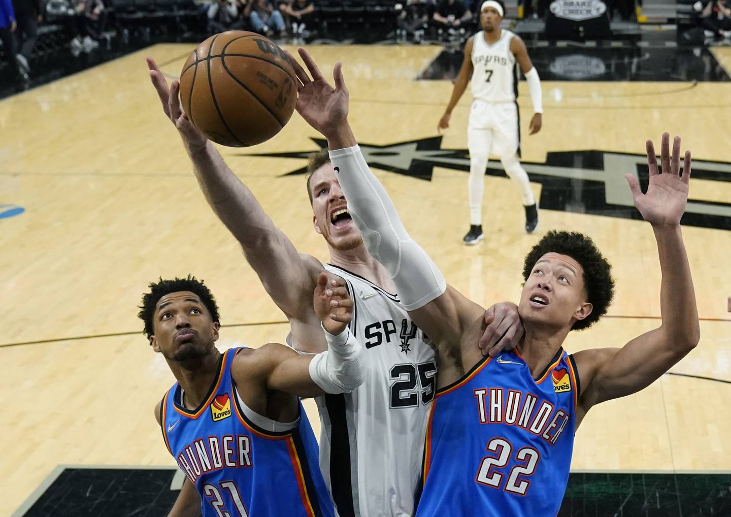San Antonio Spurs center Jakob Poeltl (25) battles Oklahoma City Thunder guard Aaron Wiggins (21) and forward Isaiah Roby (22) for a rebound during the second half Wednesday, March 16, 2022, in San Antonio. (AP Photo/Eric Gay)