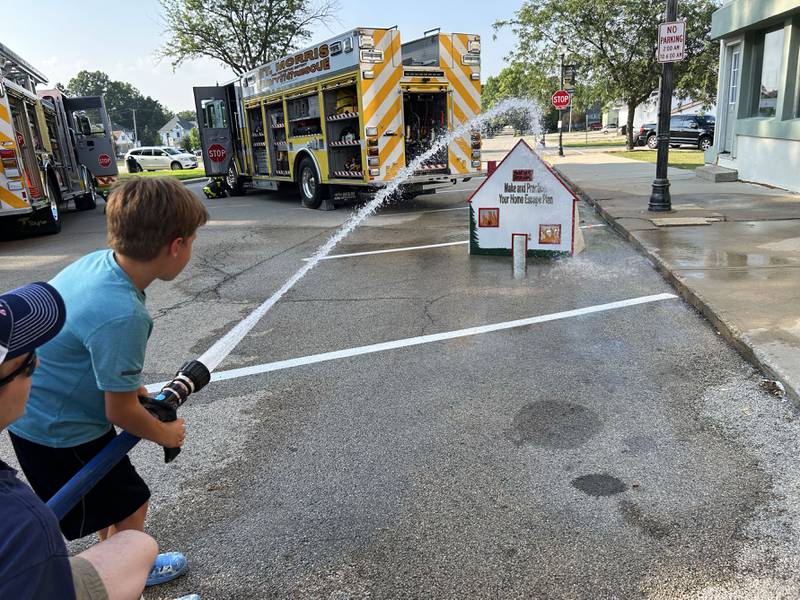 Joey Nesemeier, 8, of Mt. Morris, uses a fire hose under the direction of Mt. Morris Firefighter RG Hough at the National Night Out event in Mt. Morris on Tuesday, Aug. 5, 2025. The event was organized by the Mt. Morris Police Department.