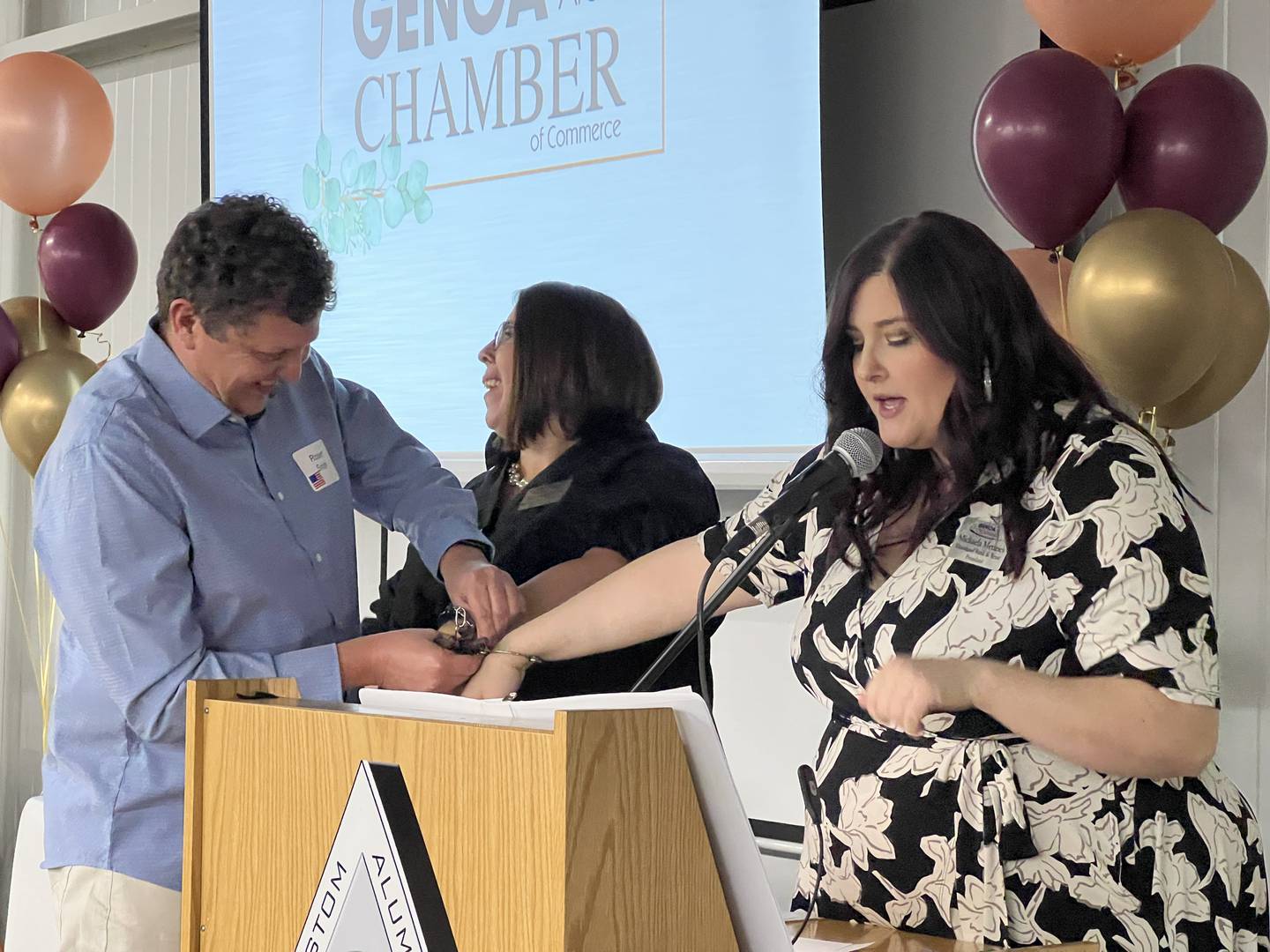 Genoa Police Chief Robert Smith helps Jennifer Groce and Michaela Menzies, who was elected president of the Genoa Area Chamber of Commerce Board of Directors during the annual dinner on Feb. 21, 2024, out of toy handcuffs as they present.