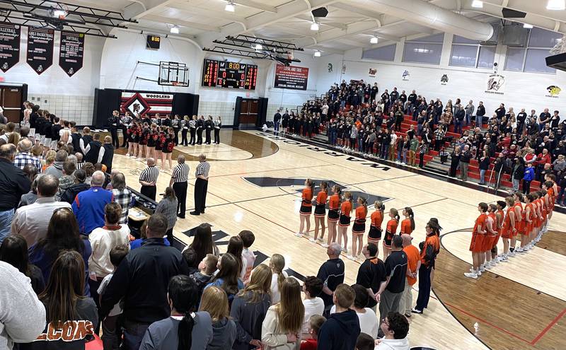 The Woodland boys basketball team, cheerleaders and Dance Force (at left) and Flanagan-Cornell cheerleaders and boys basketball team stand at attention Monday, Feb. 24, 2025, during the playing of the national anthem at the Warrior Dome in rural Streator.