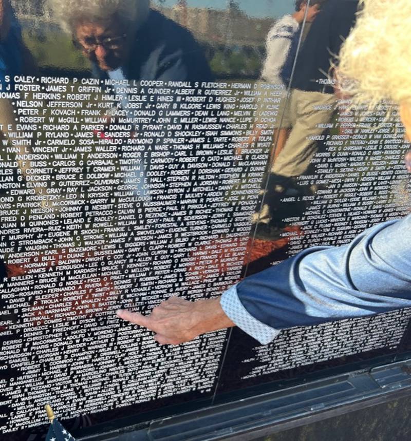 With her reflection showing in the stone wall, Diane Celletti of Rock Falls on Friday points to the name of her brother-in-law, Jerry Celletti, who was killed in the Vietnam War.