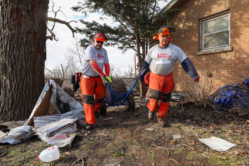 Team Rubicon members Ryan Keith, left, Army veteran, and Tony Franssens, retired Chicago firefighter, assist with debris removal in the Oakwoods subdivision in Aroma Township on March 19, 2026 following the March 10 tornado.