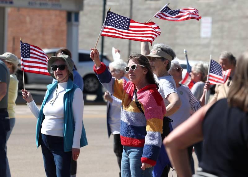 Protesters wave flags Friday, March 14, 2025, on the corner of State and Main Street in Sycamore. The group was protesting recent cuts by President Donald Trump and his administration to the Department of Veterans Affairs.