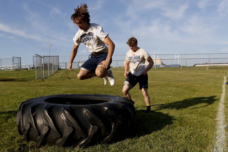 Cary-Grove’s Kyle Jarecki jumps tractor tire as Gabe Simpson prepares to flip the tire over during summer football practice Thursday, June 30, 2022, at Cary-Grove High School in Cary.