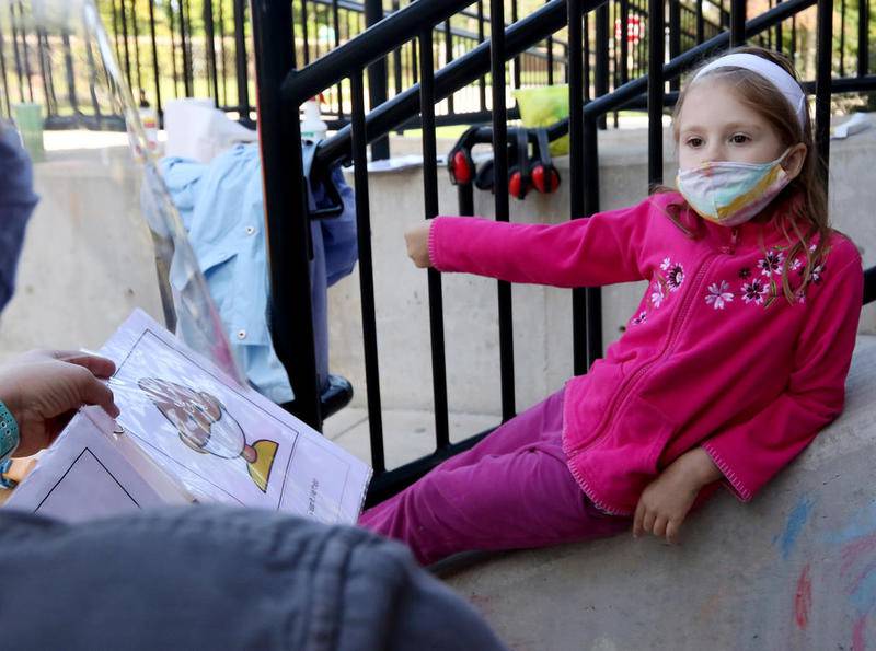Speech pathologist Valerie Kinsella (left) uses a workbook teaching the proper way to wear a face mask to a kindergartener in the district's ASPIRE (Achieving Social Pragmatics and Individual Relationships Everywhere) Program during a mask desensitization lesson Thursday at South Elementary School in Crystal Lake.