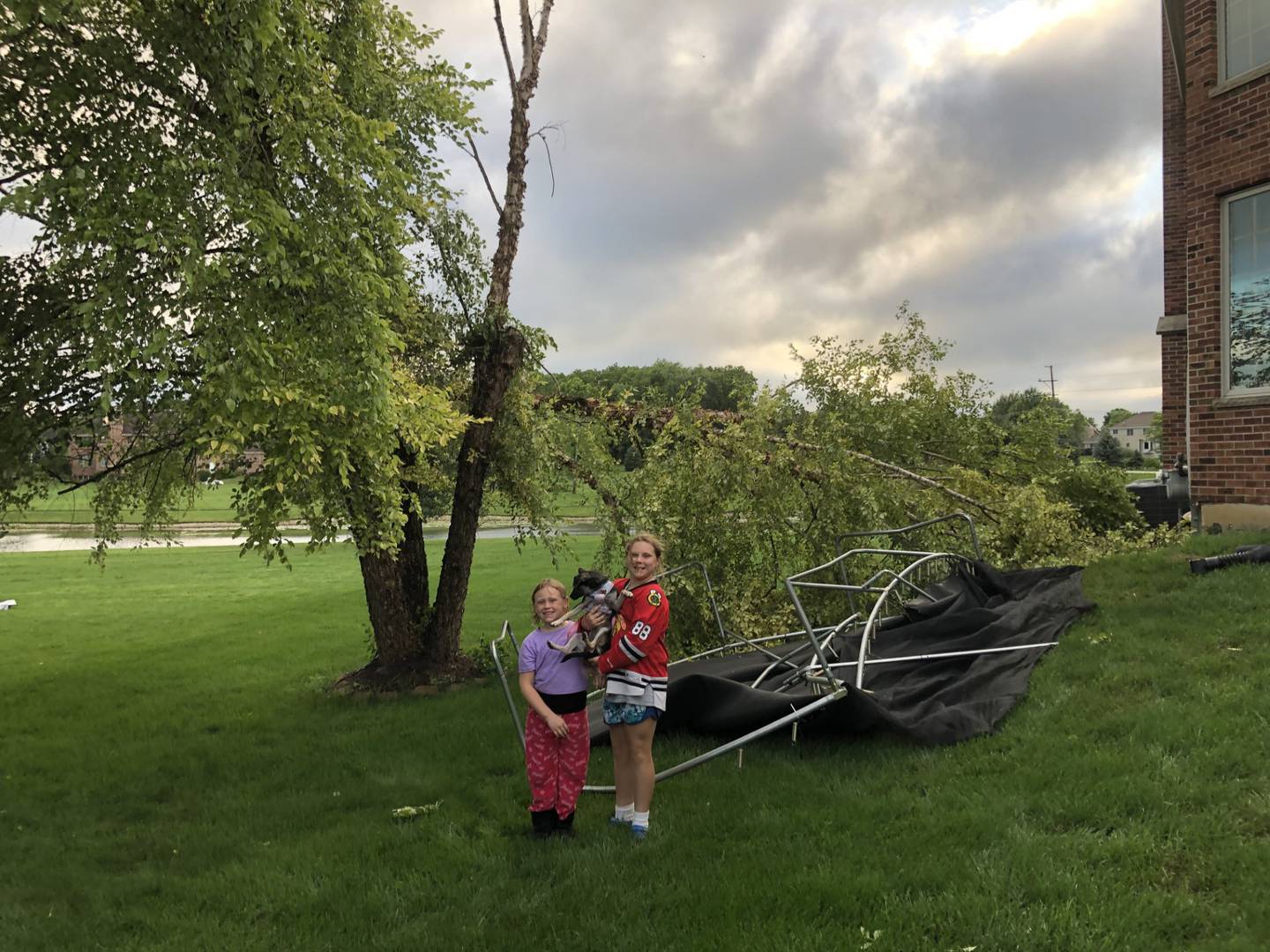 Keeley and Faith Crawmer stand near their trampoline, which was thrown into their neighbors house by a storm on the evening of June 12, 2023 on the 9N700 block of Whispering Springs Lane in Elgin.